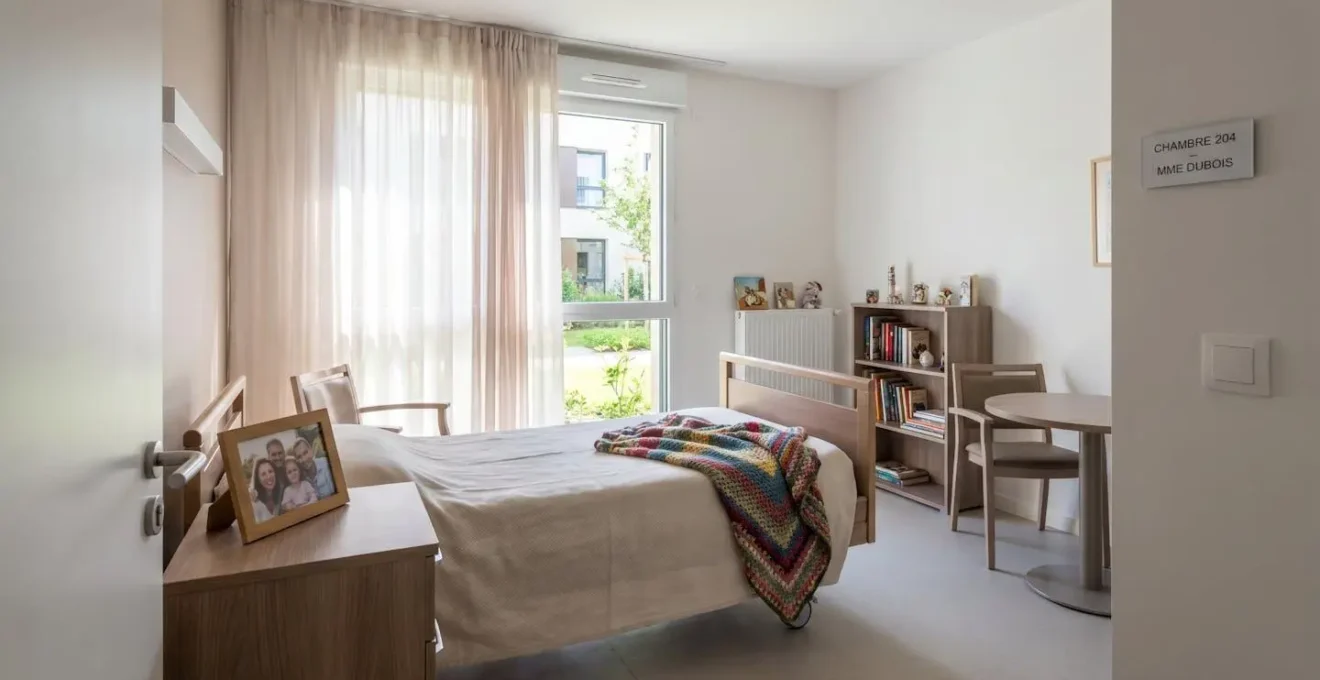 Vue d'une chambre lumineuse en EHPAD avec objets personnels sur la table de chevet et couverture colorée