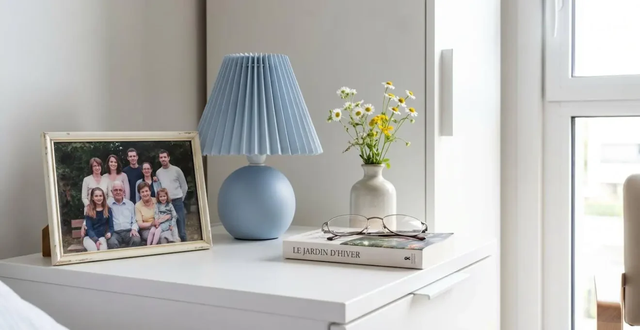 Vue rapprochée d'une table de chevet avec cadre photo familial, lampe douce et petit vase de fleurs fraîches