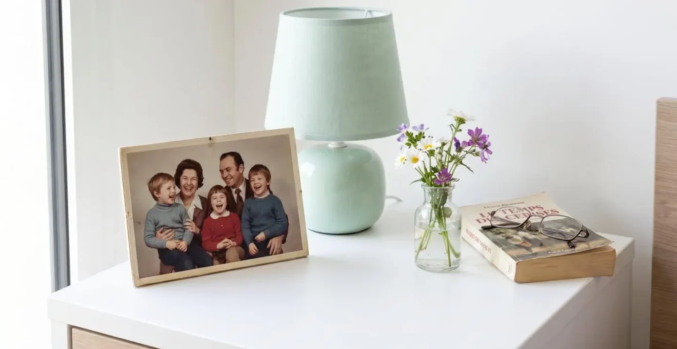 Vue rapprochée d'une table de chevet avec cadre photo familial, lampe douce et petit vase de fleurs fraîches