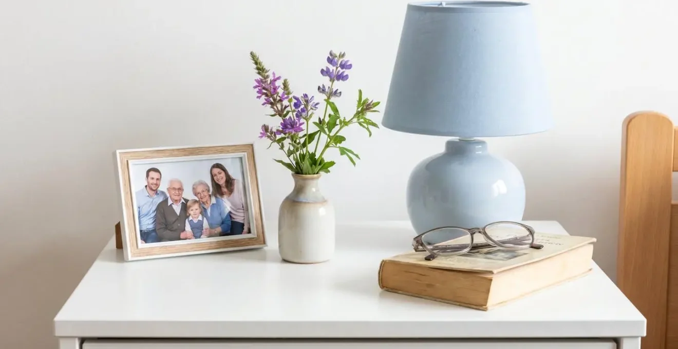 Vue rapprochée d'une table de chevet avec cadre photo familial, lampe douce et petit vase de fleurs fraîches